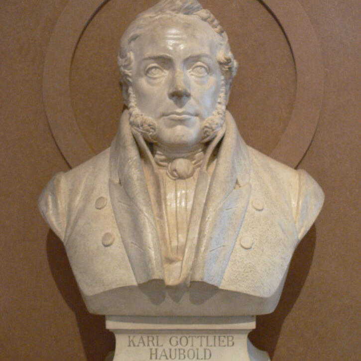 Das Bild zeigt eine helle Büste des Juristen Karl Gottlieb Haubold. Dargestellt ist der Kopf und Oberkörper eines Mannes mit kurzen Haaren und ausgeprägten Koteletten, der eine historische Kleidung mit Halstuch und Mantel trägt. Unter der Büste steht sein Name.