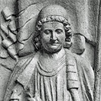 Das Bild zeigt eine steinerne Reliefdarstellung von Markgraf Dedo III. mit lockigen Haaren und Kopfbedeckung. Er ist frontal dargestellt und trägt ein Gewand mit über die Schulter gelegtem Mantel.