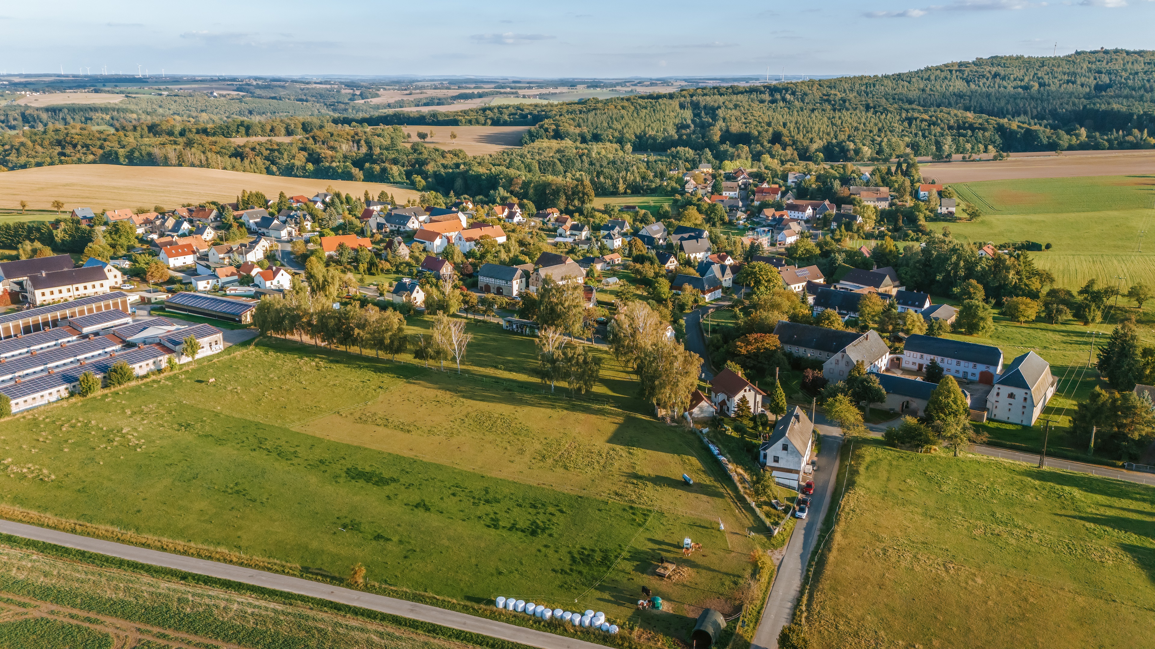 Luftaufnahme des Ortsteils Noßwitz mit dörflicher Bebauung, landwirtschaftlichen Gebäuden und Solaranlagen. Umgeben von Wiesen, Feldern und bewaldeten Hügeln zeigt das Bild die ländliche Struktur des Ortes.