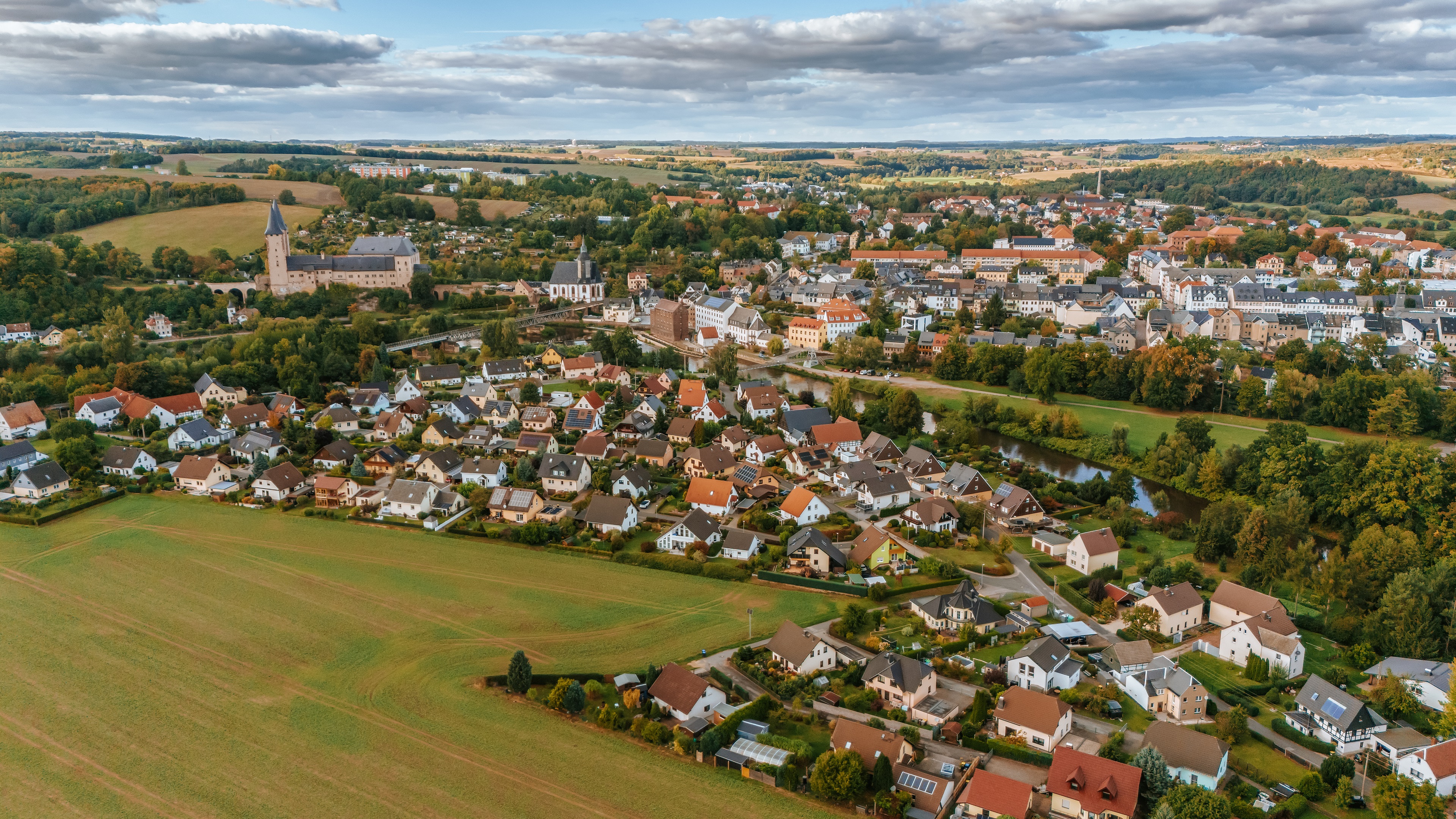 Luftaufnahme eines Wohngebiets im Ortsteil Zaßnitz. Zu sehen sind Einfamilienhäuser mit Gärten, ein Flusslauf (Zwickauer Mulde), eine historische Burganlage (Schloss Rochlitz) sowie die angrenzende Stadtstruktur von Rochlitz, eingebettet in eine hügelige Landschaft.