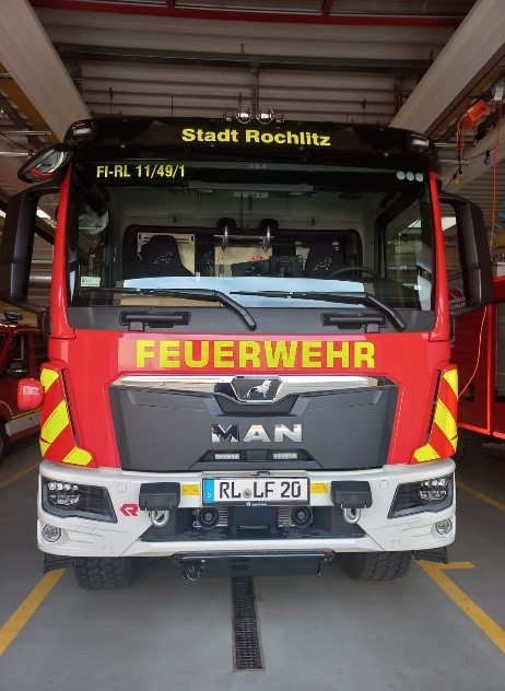 Modernes rotes Löschfahrzeug der Feuerwehr Rochlitz in einer Fahrzeughalle. Auf der Front sind die Schriftzüge ‚Feuerwehr‘ und ‚Stadt Rochlitz‘ zu sehen.