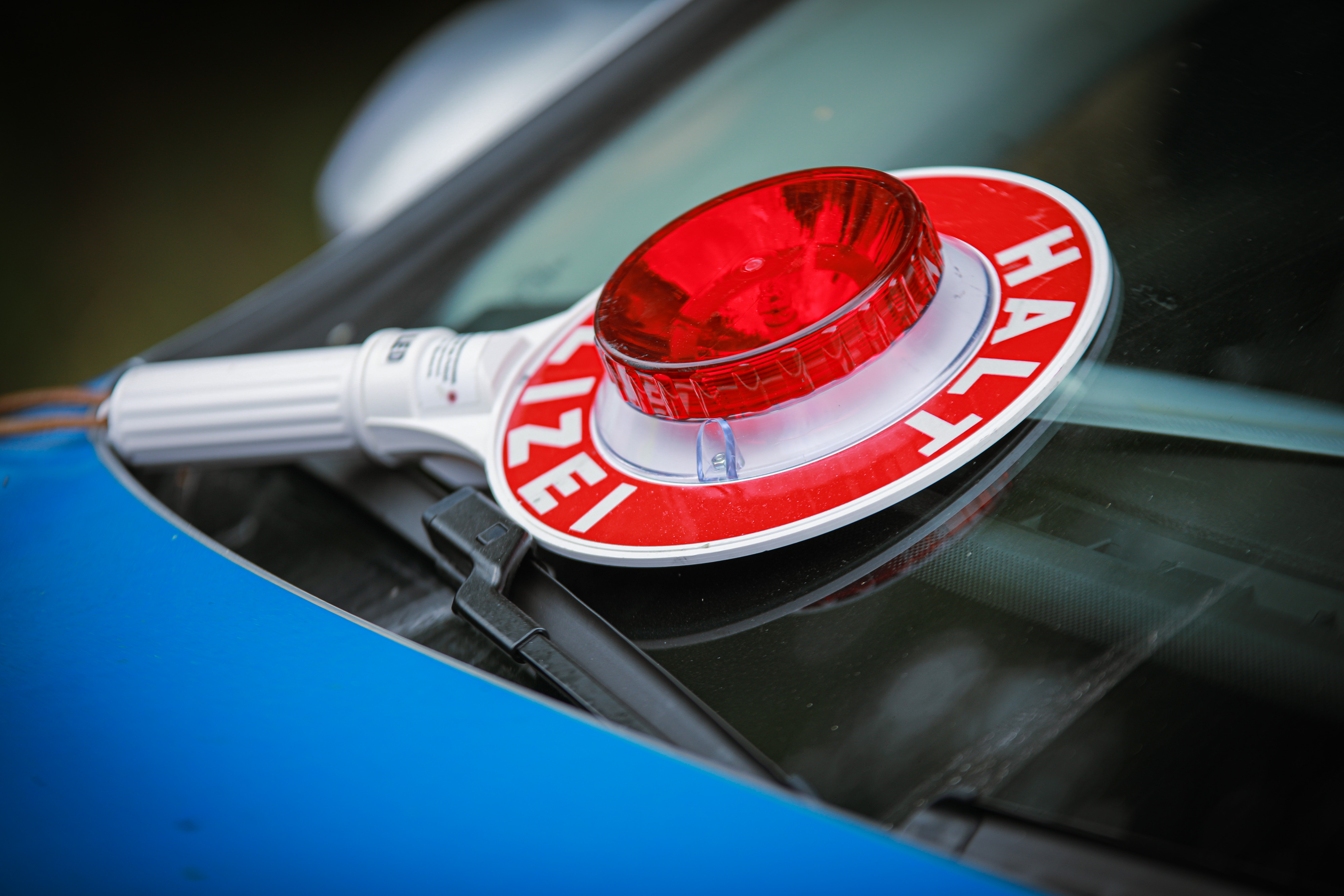 Eine rote Polizeikelle mit der Aufschrift „HALT POLIZEI“ liegt auf der Windschutzscheibe eines Polizeifahrzeugs. Die Kelle dient der Verkehrsregelung und zum Anhalten von Fahrzeugen.