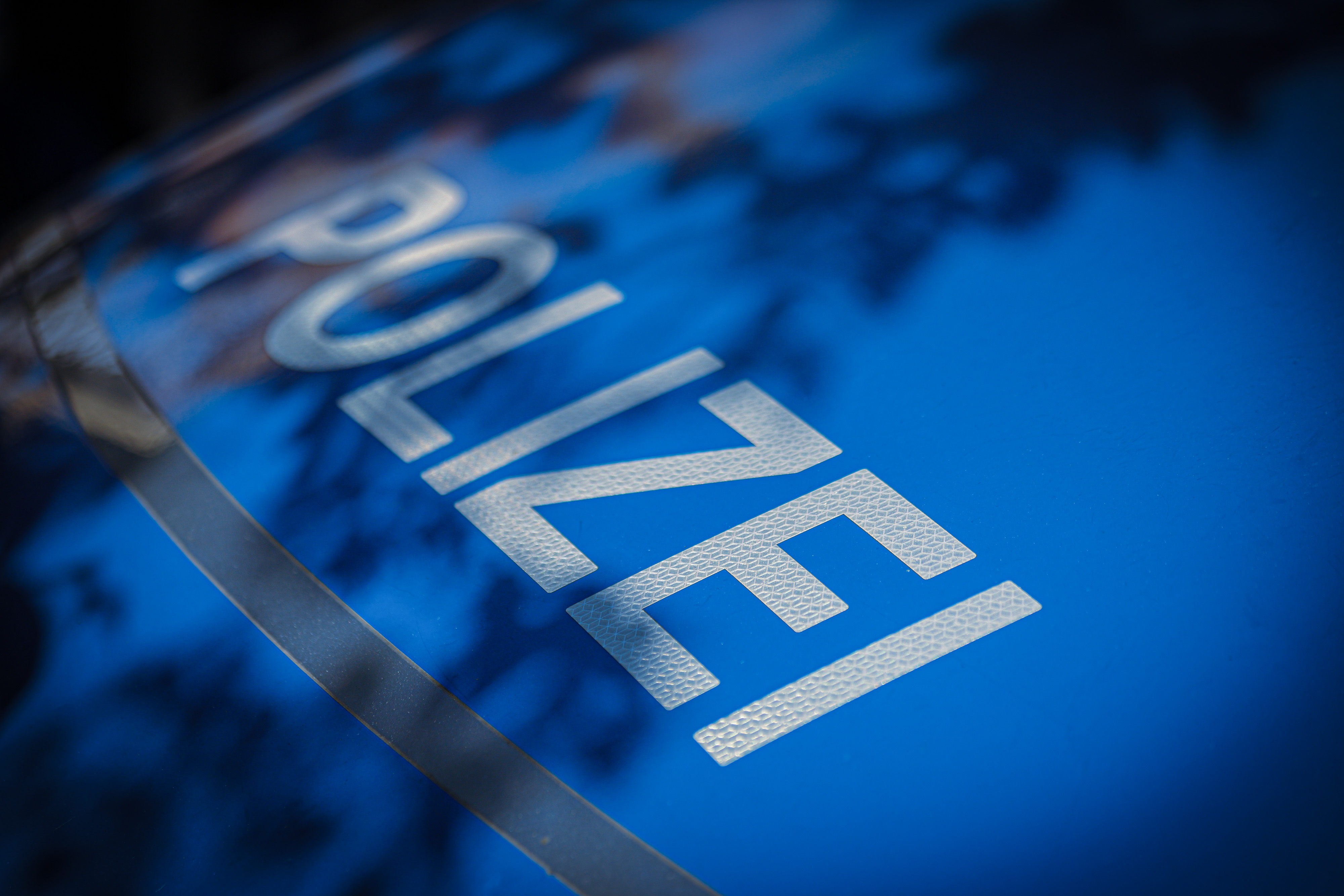 Detailaufnahme des Schriftzugs „POLIZEI“ auf der Motorhaube eines Polizeifahrzeugs. Die weißen Buchstaben sind auf blauem Hintergrund angebracht.